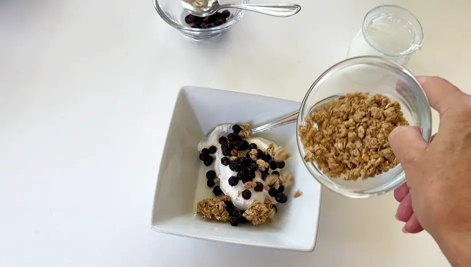 adding granola and blueberries to yogurt